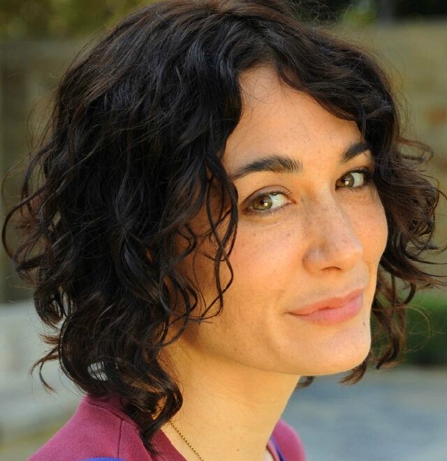 Portrait of Miki Huber Wood, smiling, with dark curly hair